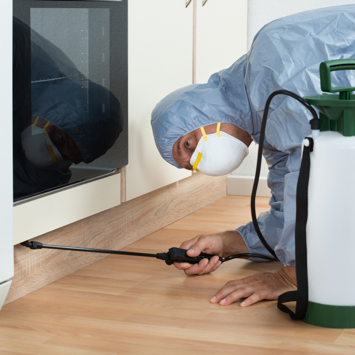 Man kneeling on floor wearing proctieve cleaning gear spraying under cabinets