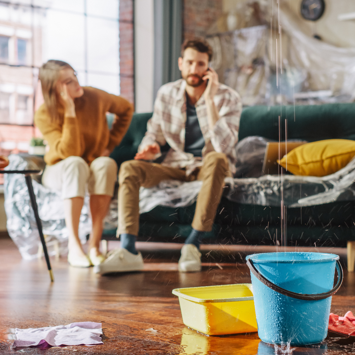 Man and woman in the background while leak is caught by a bucket in the foreground