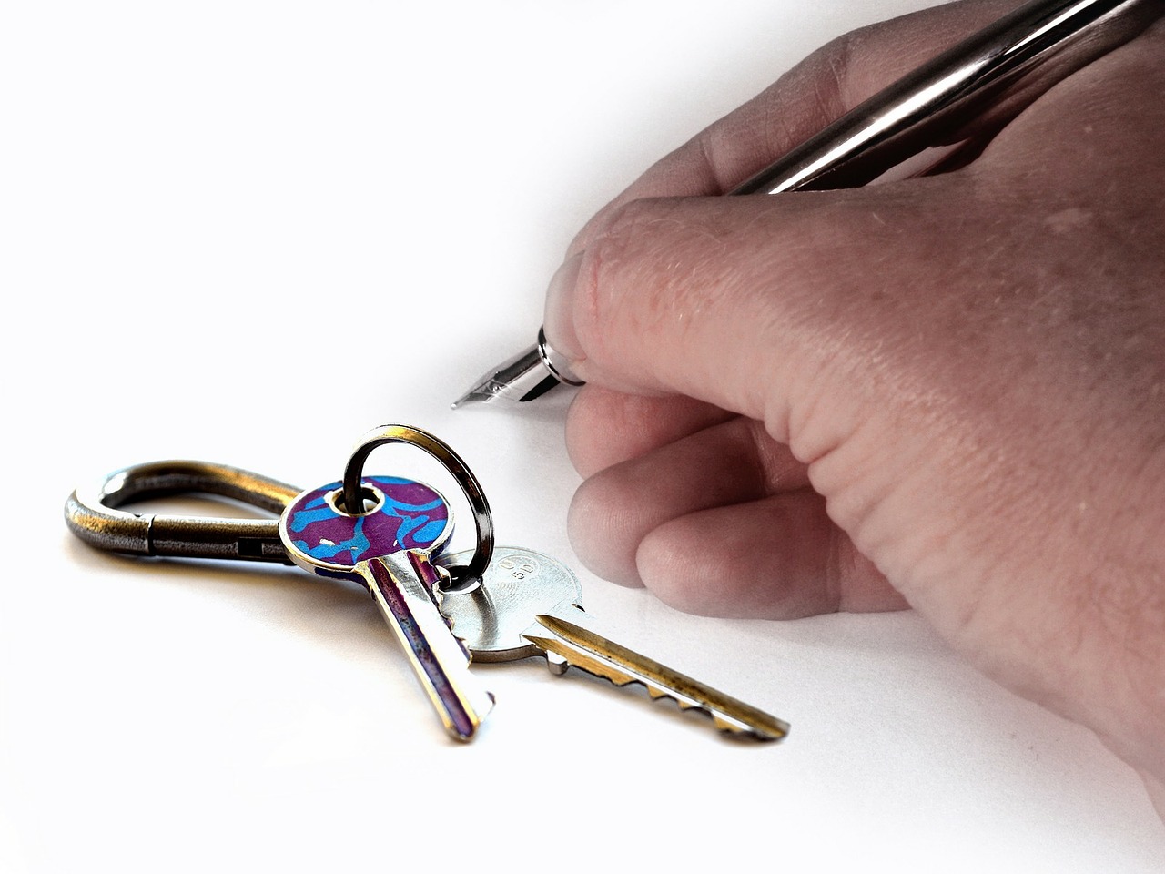 House keys next to a hand holding a pn writing on a document