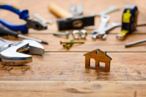 Small figurine of a house on the background of construction tools on a wooden table. House construction and renovation concept. Selective focus on a small house.