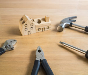 Set of manual house tools on a wooden table.They surround a handmade wood house toy.