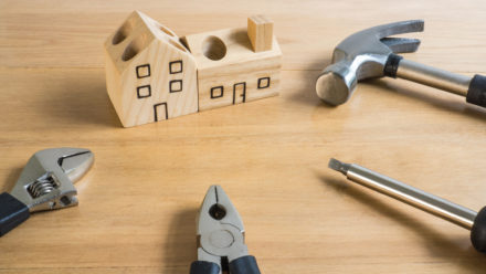 Set of manual house tools on a wooden table.They surround a handmade wood house toy.