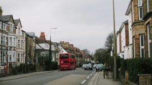 London residential street with a red double decker bus driving down it